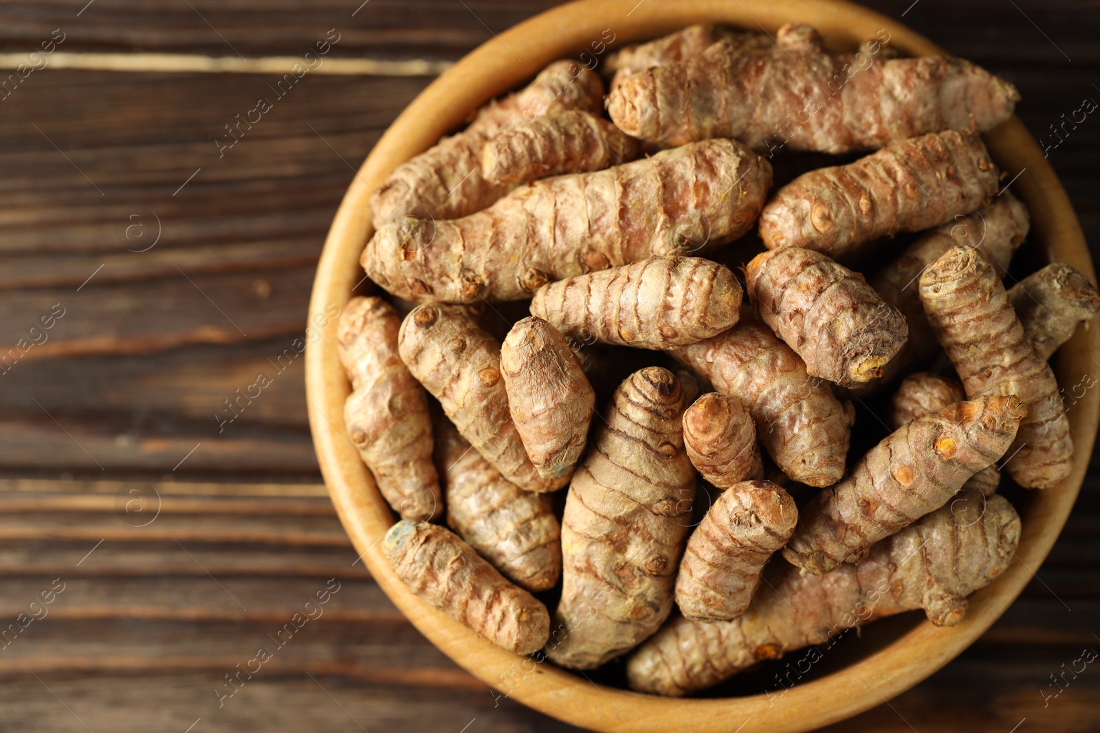 Photo of Tumeric rhizomes in bowl on wooden table, top view