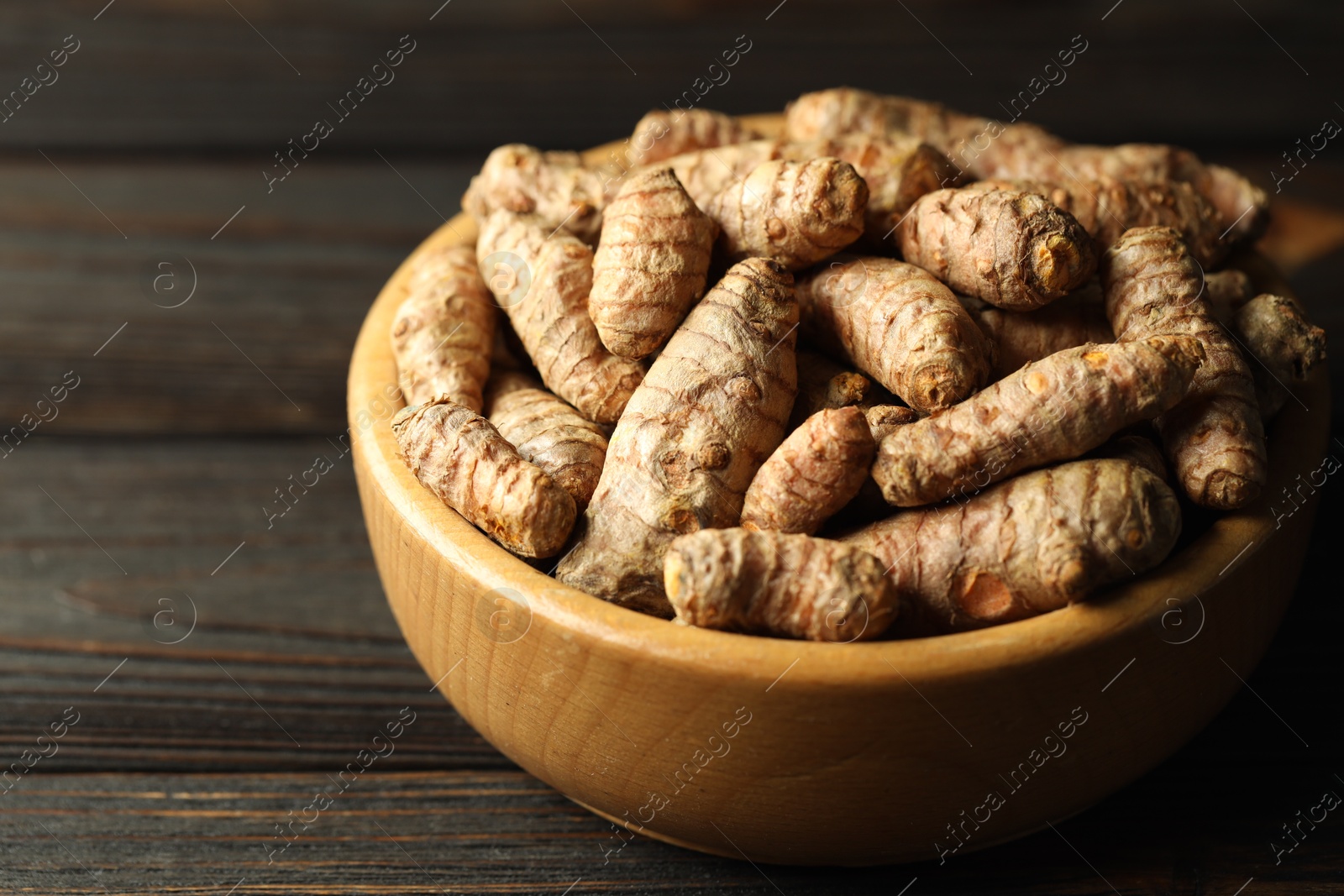 Photo of Tumeric rhizomes in bowl on wooden table, closeup