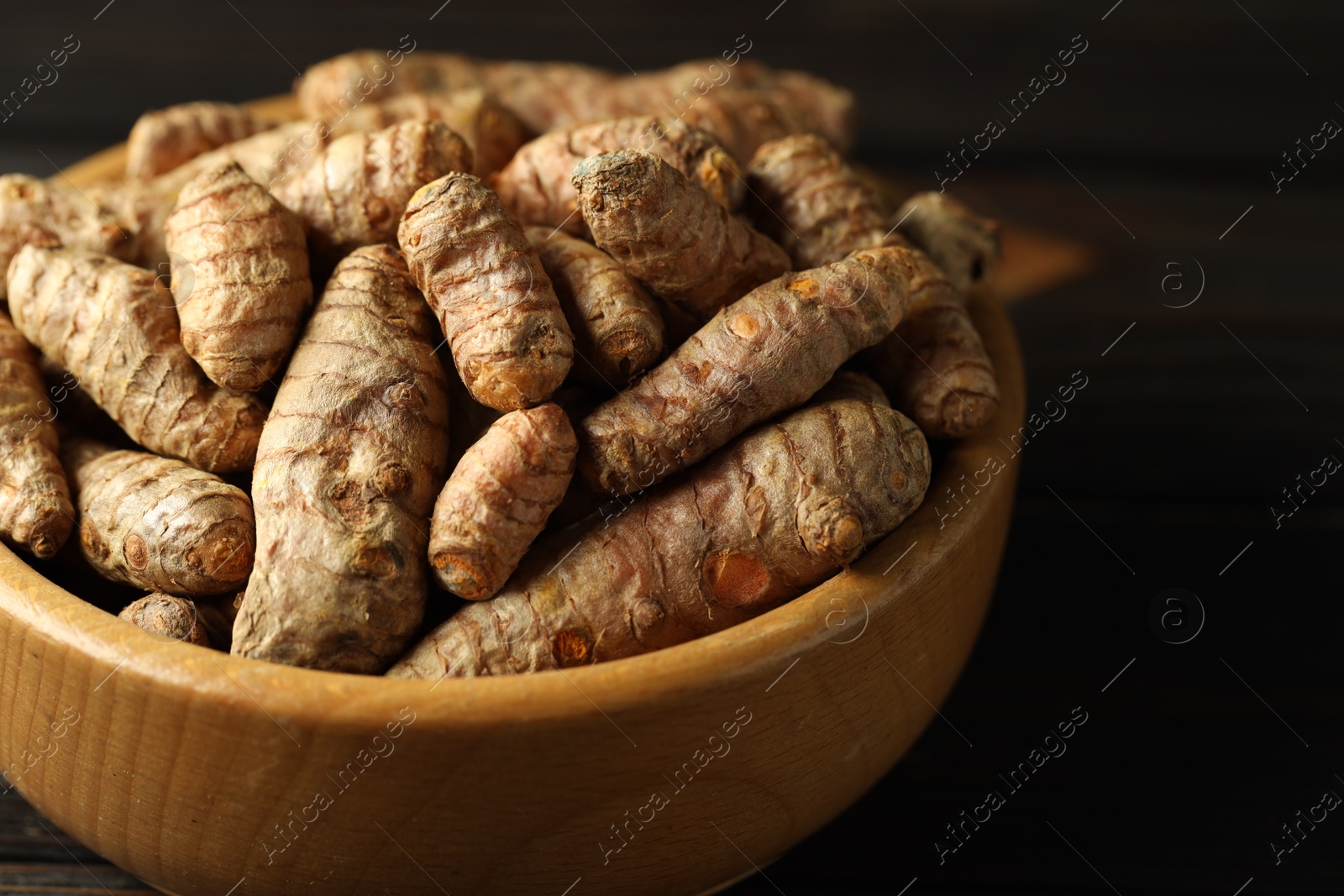 Photo of Tumeric rhizomes in bowl on wooden table, closeup