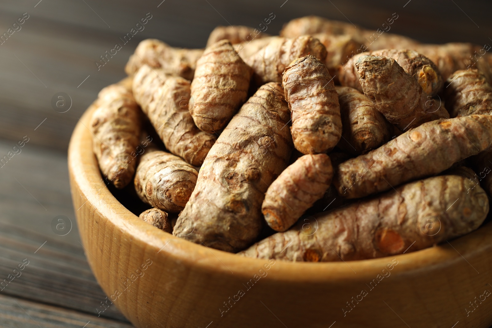 Photo of Tumeric rhizomes in bowl on wooden table, closeup