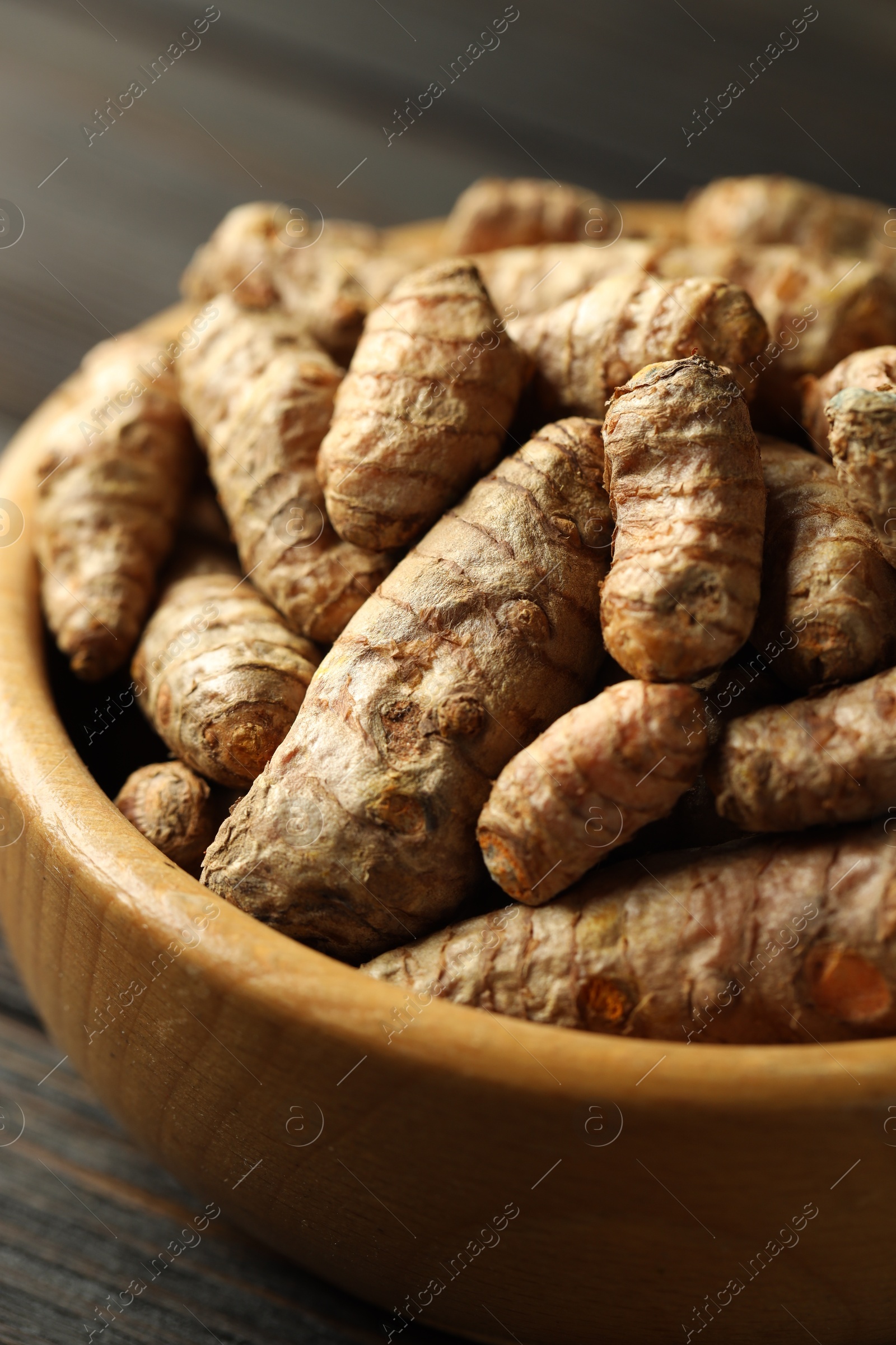 Photo of Tumeric rhizomes in bowl on wooden table, closeup