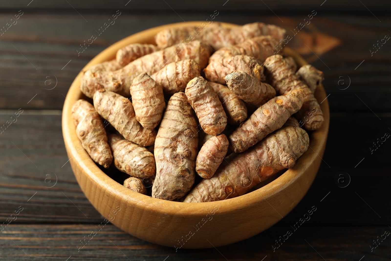 Photo of Tumeric rhizomes in bowl on wooden table, closeup