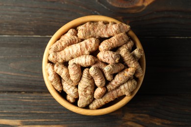 Photo of Tumeric rhizomes in bowl on wooden table, top view