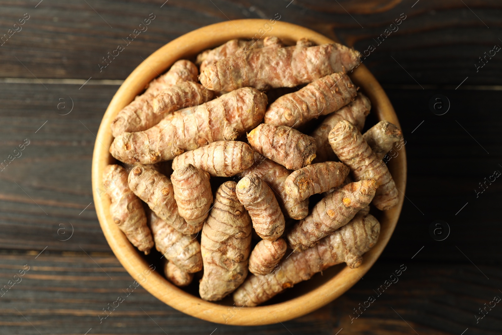 Photo of Tumeric rhizomes in bowl on wooden table, top view