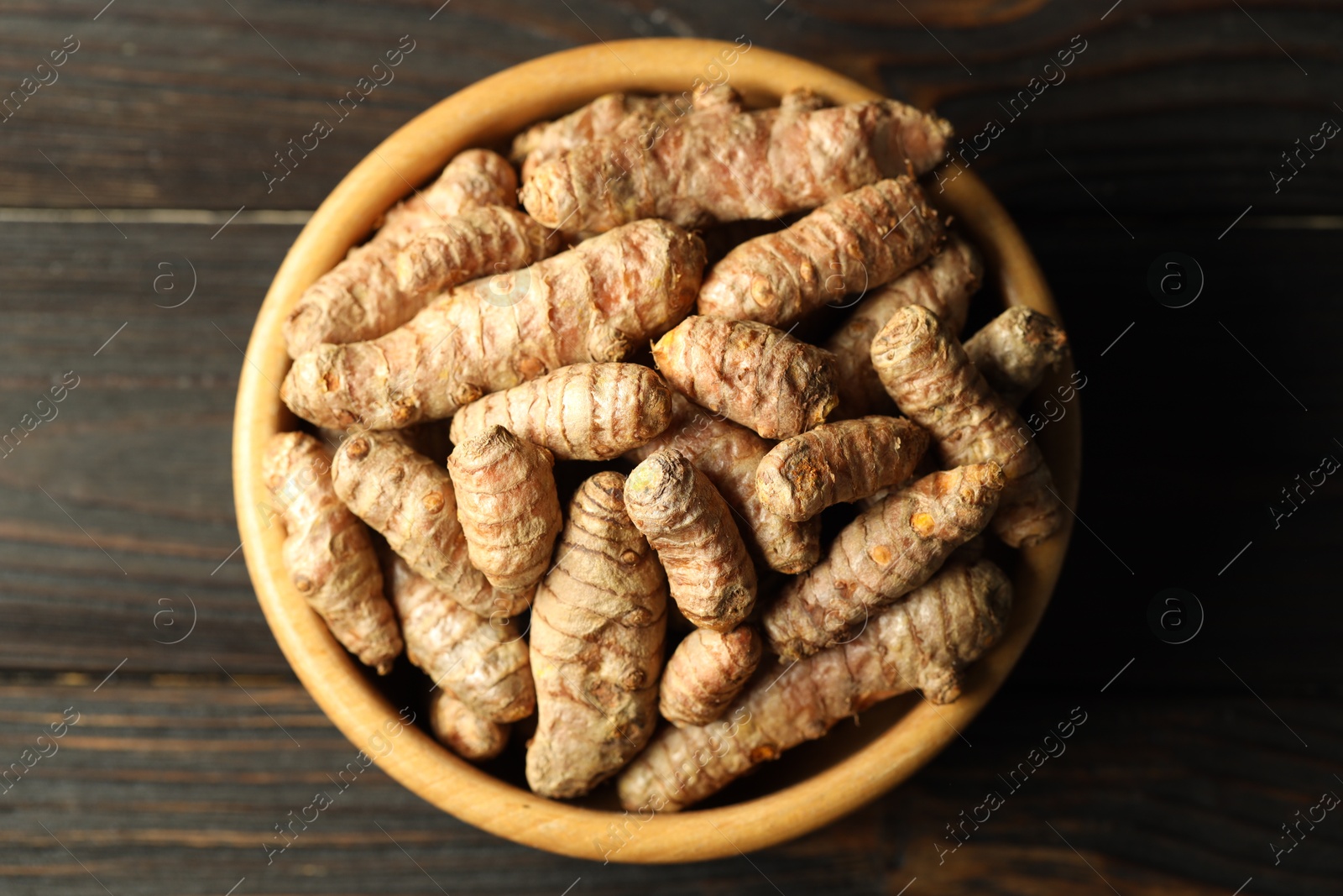 Photo of Tumeric rhizomes in bowl on wooden table, top view