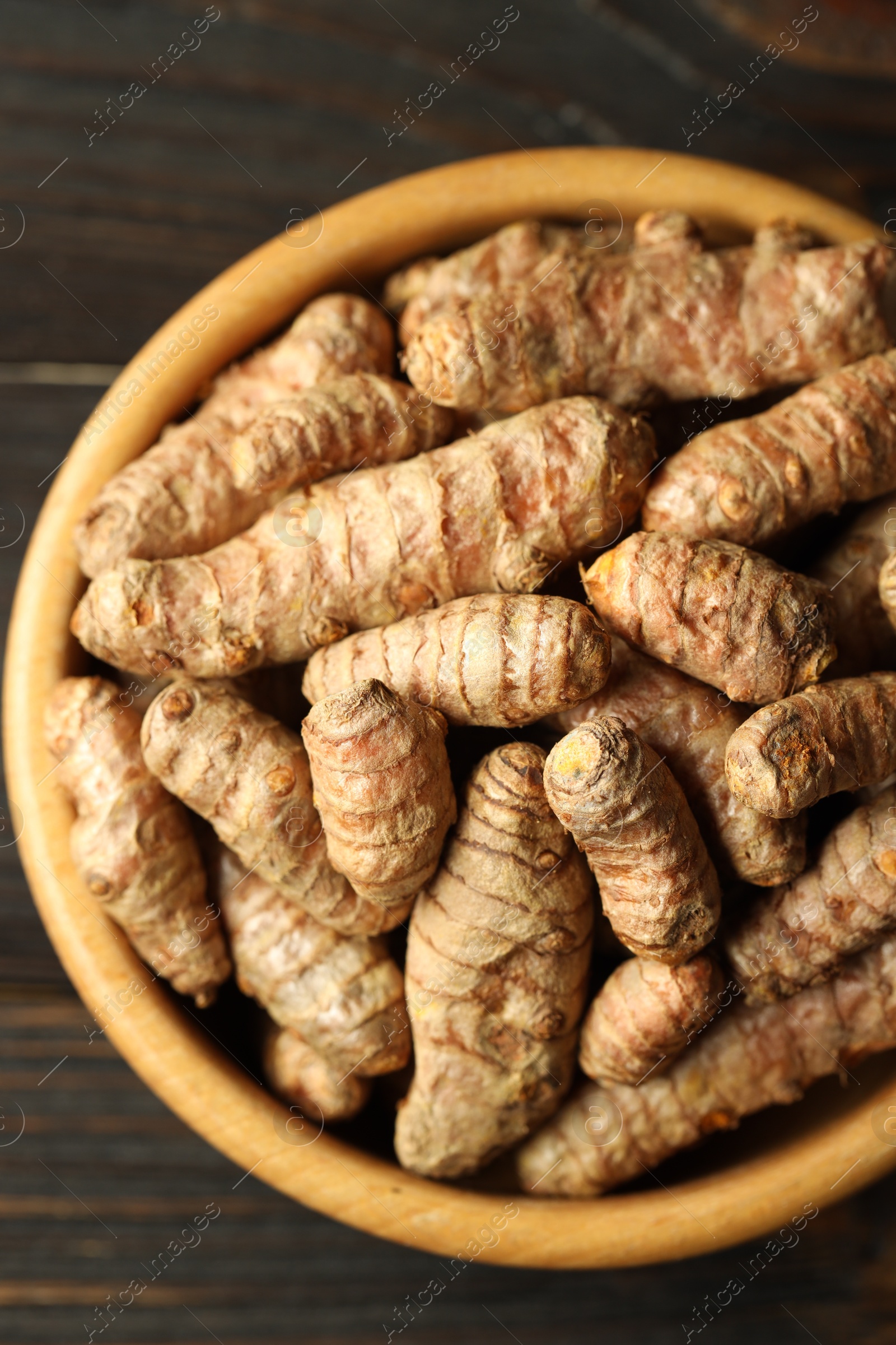 Photo of Tumeric rhizomes in bowl on wooden table, top view