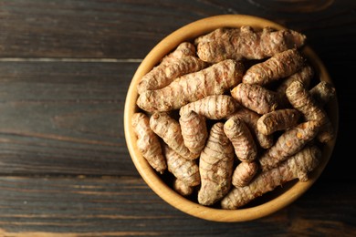 Photo of Tumeric rhizomes in bowl on wooden table, top view. Space for text