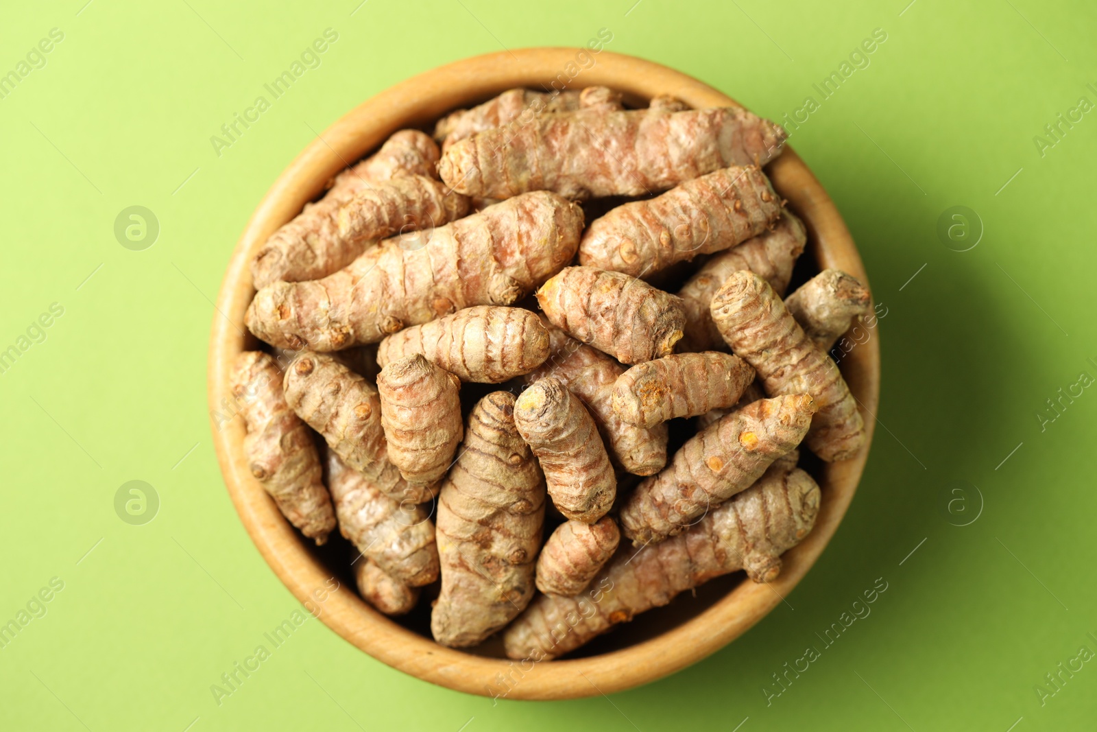 Photo of Tumeric rhizomes in bowl on green background, top view