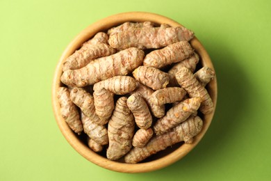 Photo of Tumeric rhizomes in bowl on green background, top view