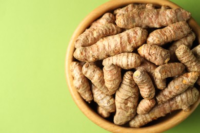 Photo of Tumeric rhizomes in bowl on green background, top view