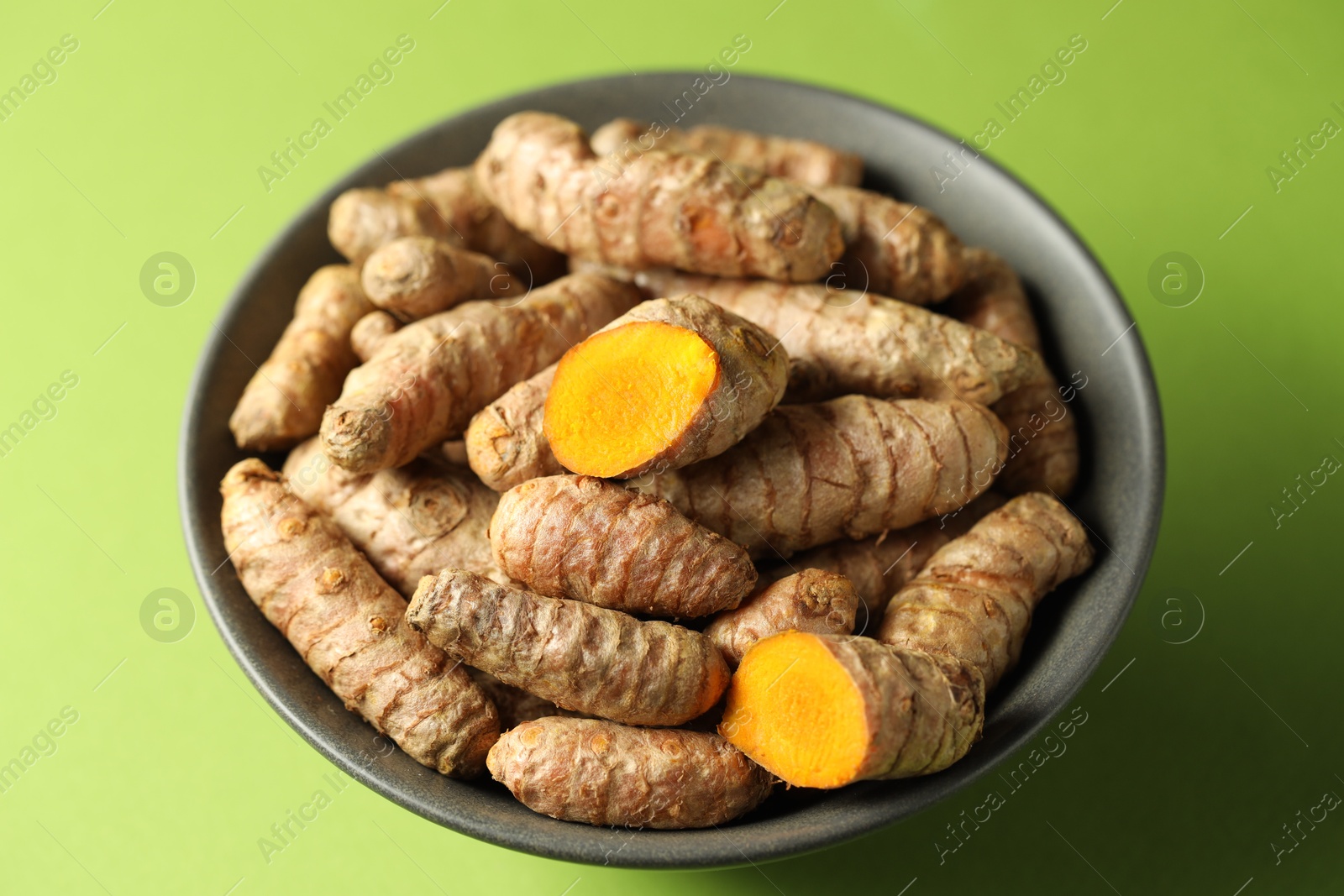 Photo of Tumeric rhizomes in bowl on green background, closeup