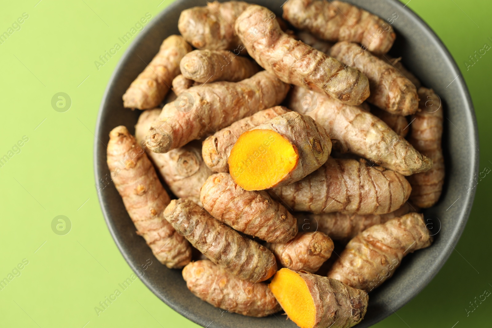 Photo of Tumeric rhizomes in bowl on green background, top view