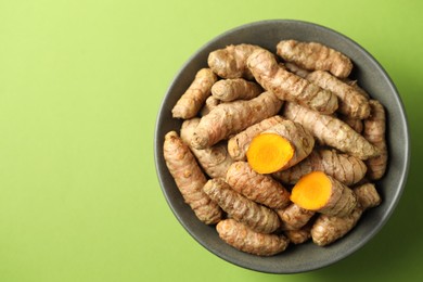 Photo of Tumeric rhizomes in bowl on green background, top view. Space for text