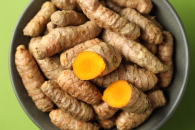 Photo of Tumeric rhizomes in bowl on green background, top view