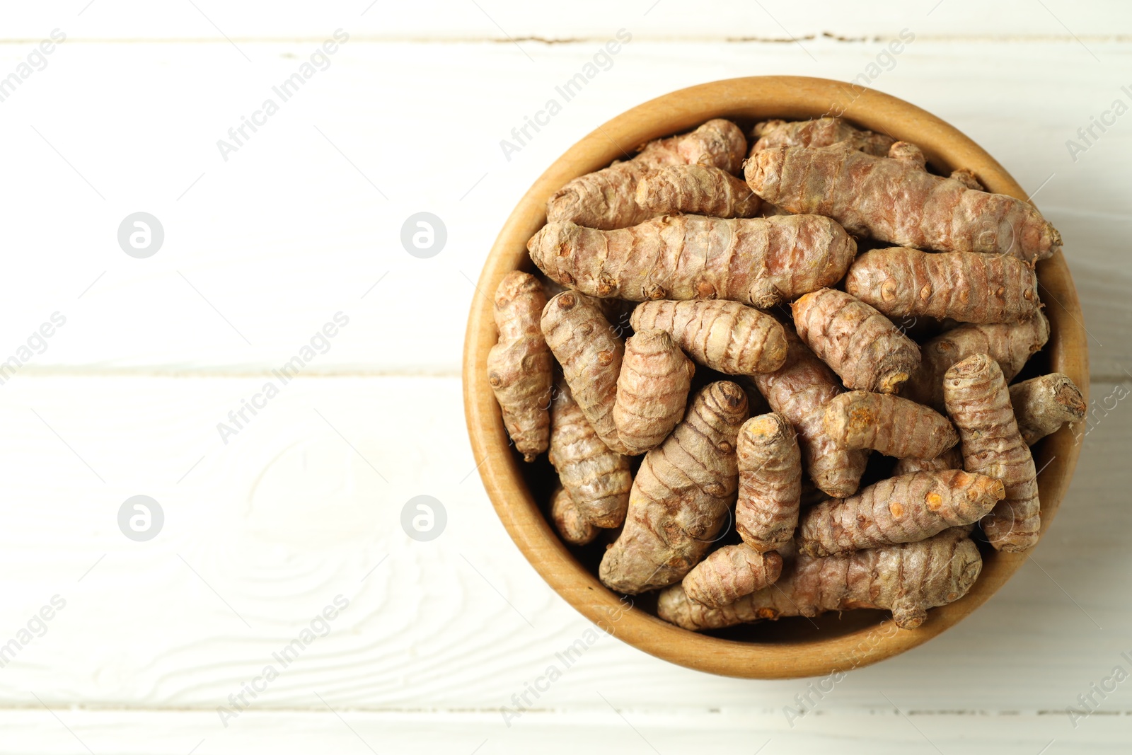 Photo of Tumeric rhizomes in bowl on white wooden table, top view. Space for text