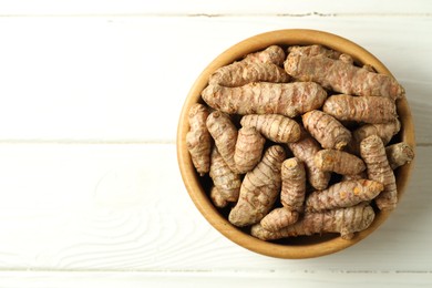 Photo of Tumeric rhizomes in bowl on white wooden table, top view. Space for text