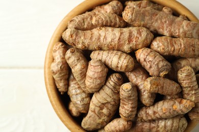 Photo of Tumeric rhizomes in bowl on white wooden table, top view