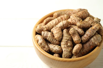 Photo of Tumeric rhizomes in bowl on white wooden table, closeup