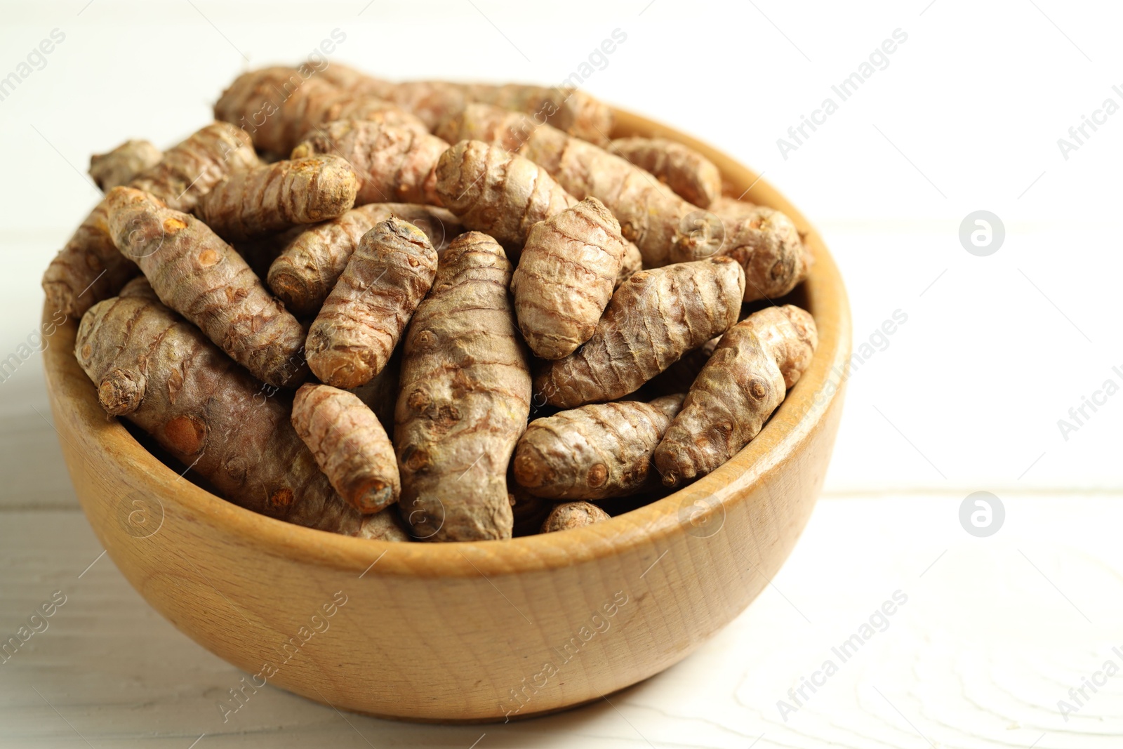 Photo of Tumeric rhizomes in bowl on white wooden table, closeup