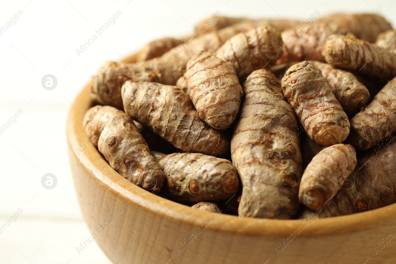 Photo of Tumeric rhizomes in bowl on white wooden table, closeup