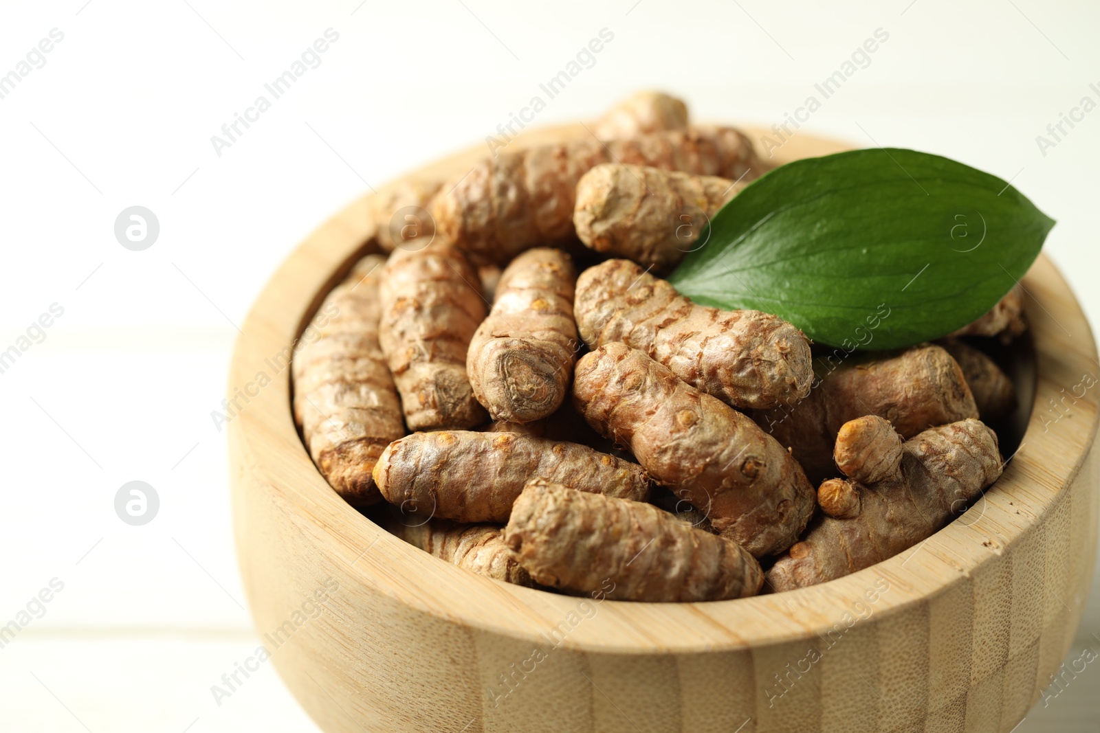 Photo of Tumeric rhizomes with leaf in bowl on white wooden table, closeup