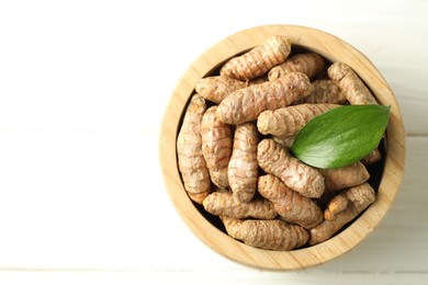 Photo of Tumeric rhizomes with leaf in bowl on white wooden table, top view. Space for text