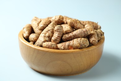 Photo of Tumeric rhizomes in bowl on light blue background, closeup