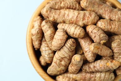 Photo of Tumeric rhizomes in bowl on light blue background, top view