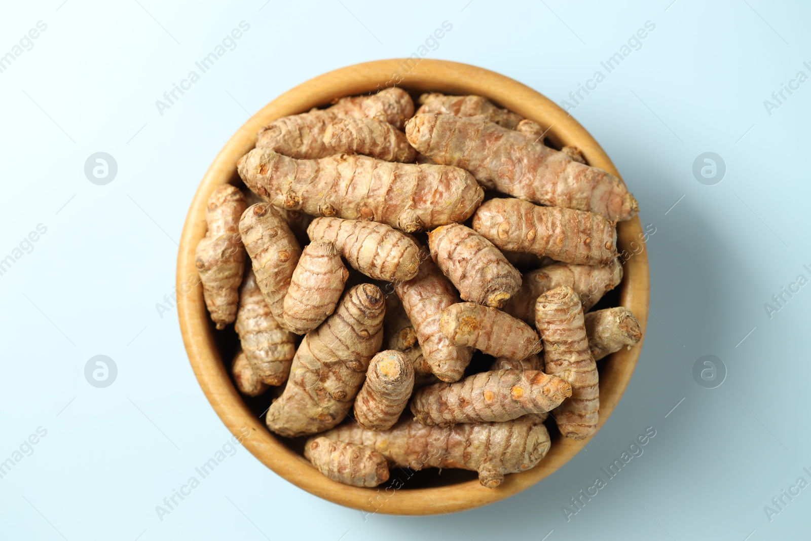 Photo of Tumeric rhizomes in bowl on light blue background, top view