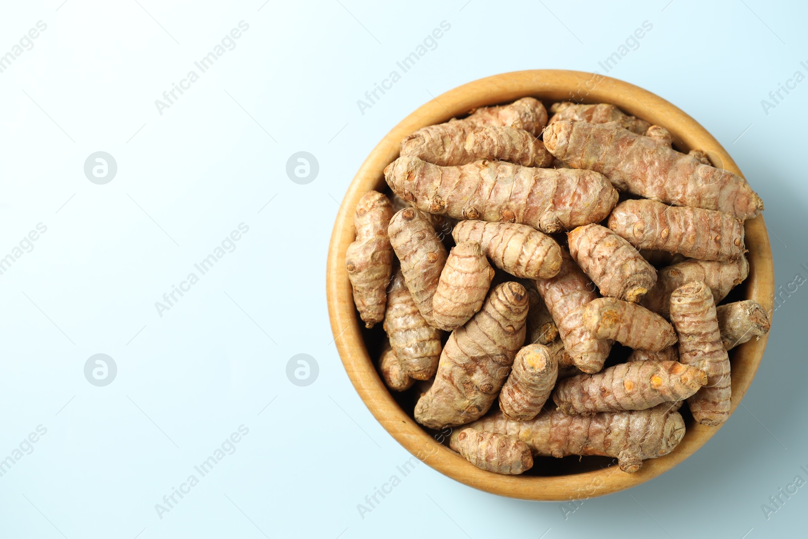 Photo of Tumeric rhizomes in bowl on light blue background, top view. Space for text