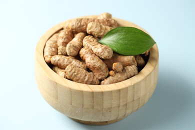 Photo of Tumeric rhizomes with leaf in bowl on light blue background, closeup