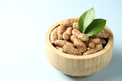 Photo of Tumeric rhizomes with leaves in bowl on light blue background, closeup. Space for text