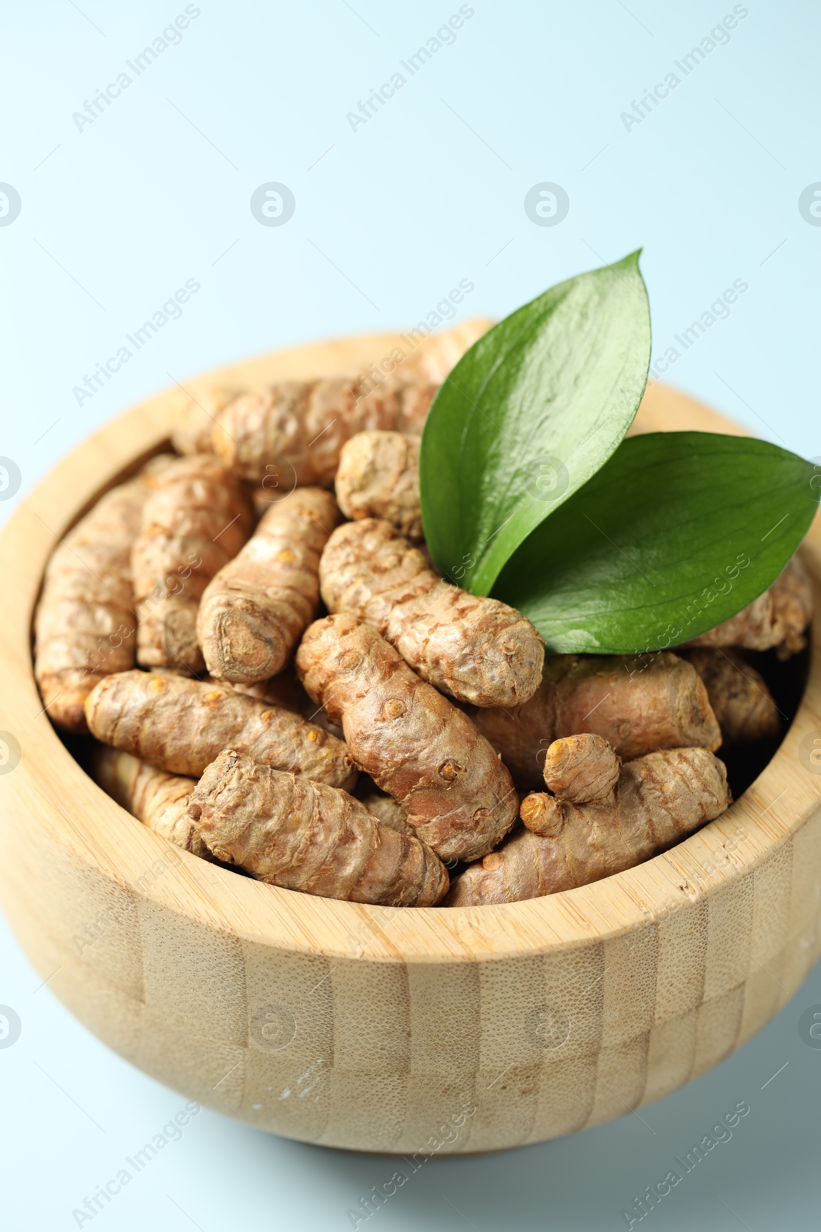 Photo of Tumeric rhizomes with leaves in bowl on light blue background, closeup