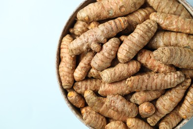 Photo of Tumeric rhizomes in bowl on light blue background, top view