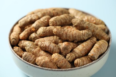 Photo of Tumeric rhizomes in bowl on light blue background, closeup