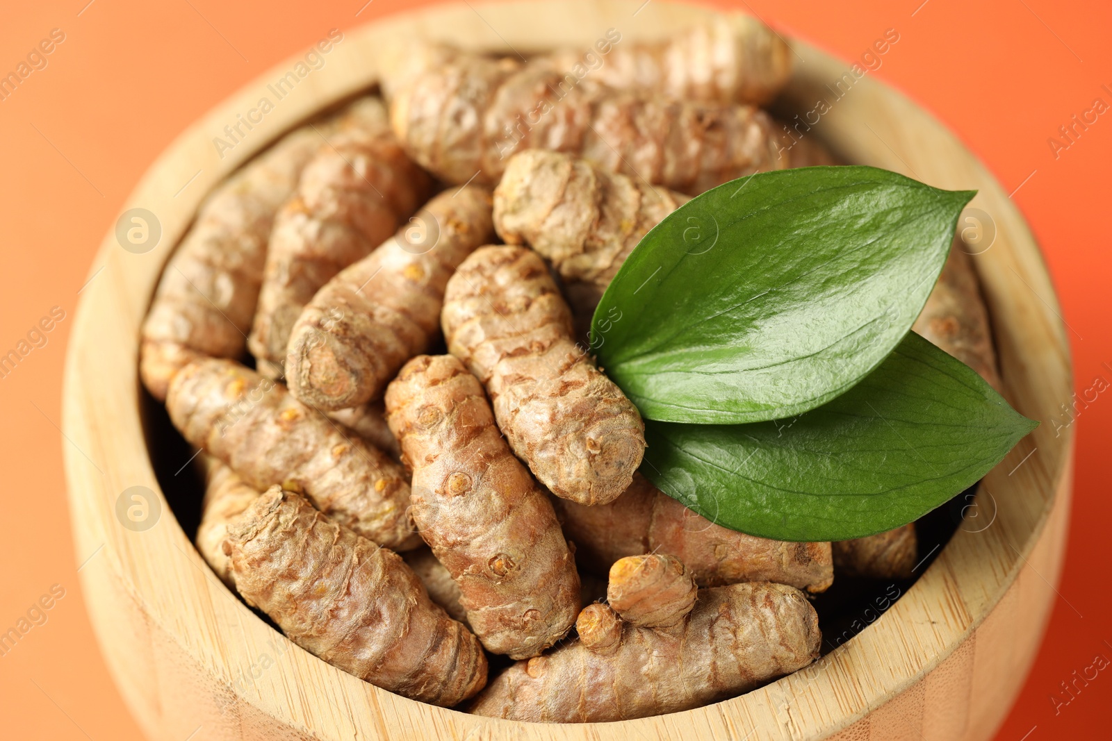 Photo of Tumeric rhizomes with leaves in bowl on orange background, closeup