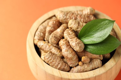 Photo of Tumeric rhizomes with leaves in bowl on orange background, closeup