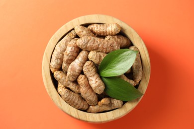 Photo of Tumeric rhizomes with leaves in bowl on orange background, top view