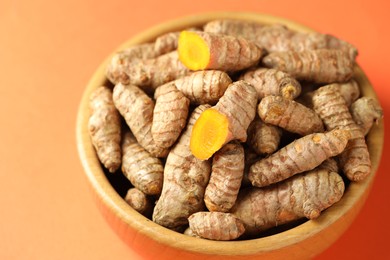 Photo of Tumeric rhizomes in bowl on orange background, closeup