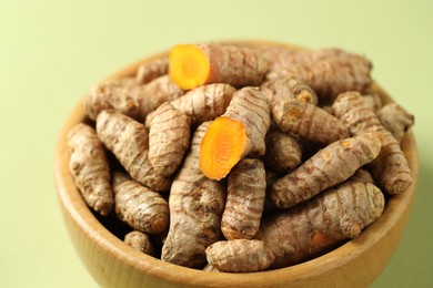 Photo of Tumeric rhizomes in bowl on light green background, closeup