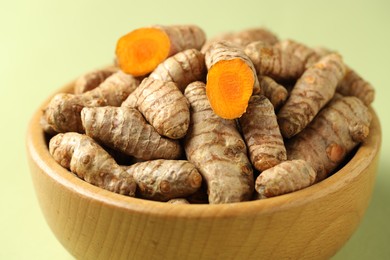 Photo of Tumeric rhizomes in bowl on light green background, closeup