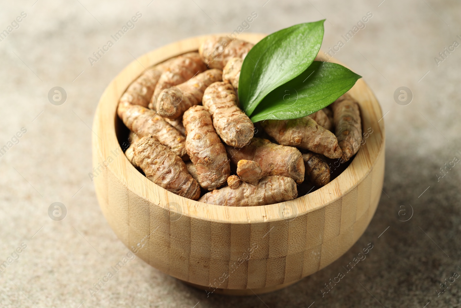 Photo of Tumeric rhizomes with leaves in bowl on grey table, closeup