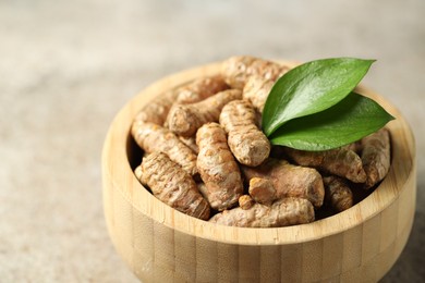 Photo of Tumeric rhizomes with leaves in bowl on grey table, closeup