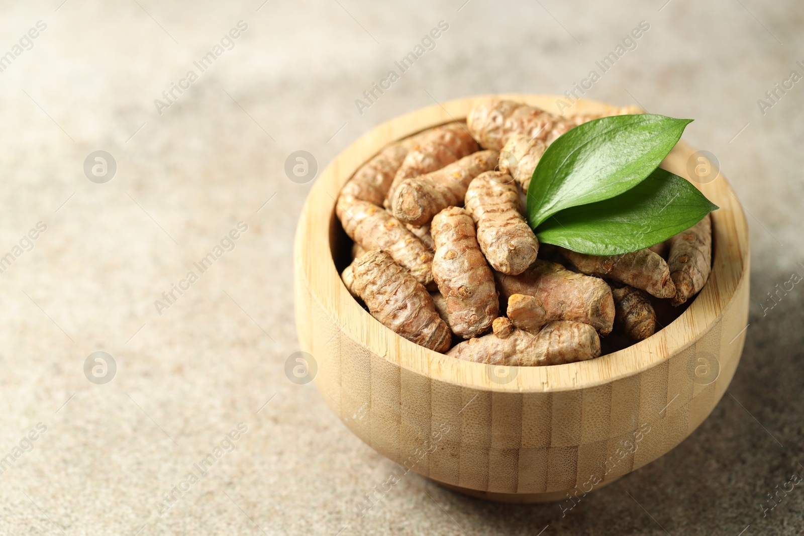 Photo of Tumeric rhizomes with leaves in bowl on grey table, closeup. Space for text