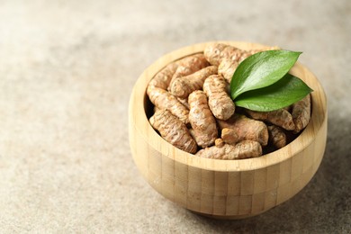 Photo of Tumeric rhizomes with leaves in bowl on grey table, closeup. Space for text