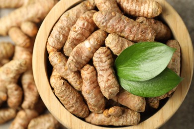 Photo of Tumeric rhizomes with leaves in bowl on table, closeup