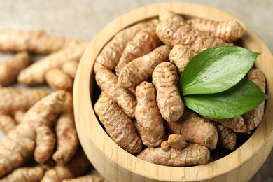 Photo of Tumeric rhizomes with leaves in bowl on grey table, closeup