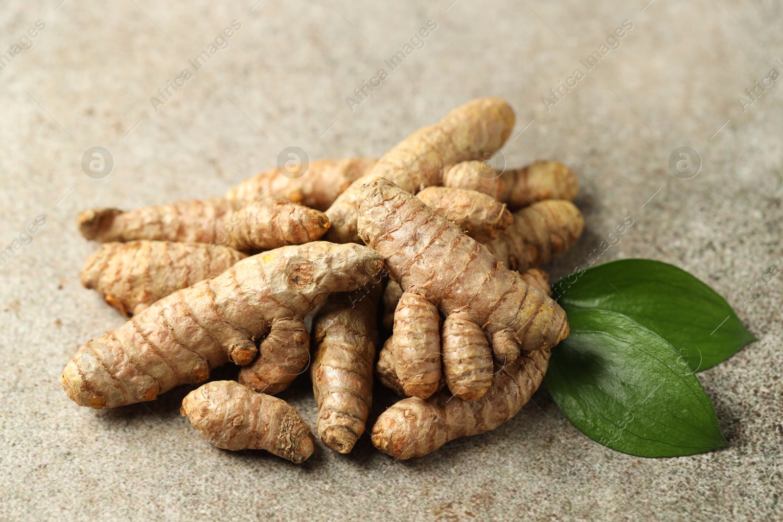 Photo of Pile of tumeric rhizomes with leaves on grey table, closeup