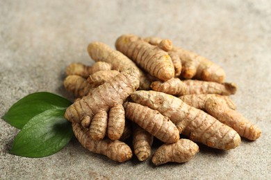 Photo of Pile of tumeric rhizomes with leaves on grey table, closeup