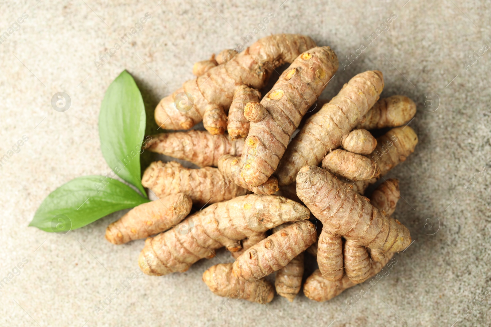 Photo of Pile of tumeric rhizomes with leaves on grey table, top view